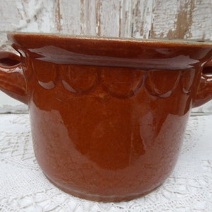 May include: A brown ceramic pot with two handles and a scalloped rim. The pot is glazed and has a shiny finish.
