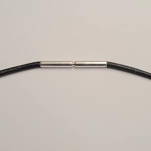 May include: A close-up of a black leather necklace cord with a silver-colored clasp. The cord is round and appears to be approximately 2 mm in diameter. The clasp is made of two cylindrical pieces that connect in the center.