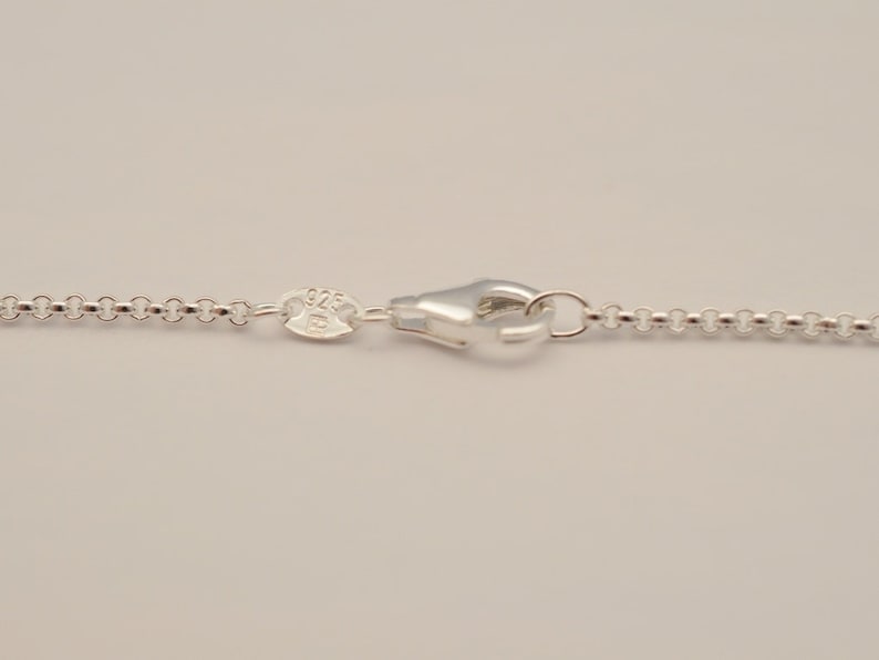 May include: Close-up of a silver necklace chain with a lobster clasp. The chain is made of small, round links. The clasp is shiny and reflective. The necklace is likely made of sterling silver, as indicated by the "925" stamp.