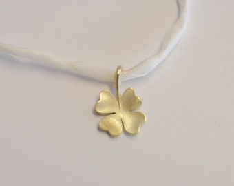 Op de afbeelding: Een gouden klavertje vier hanger aan een wit lint.