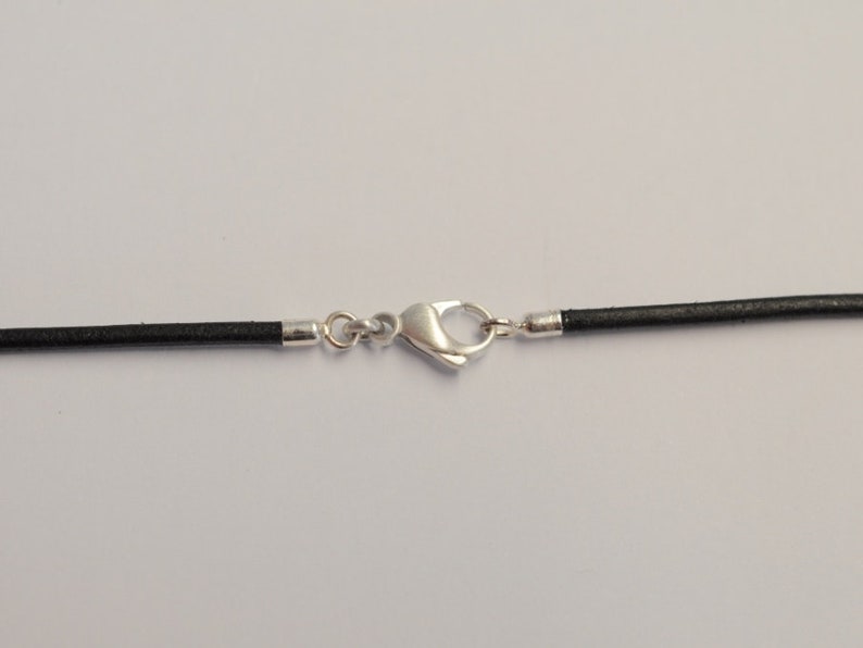May include: A black leather cord necklace with a silver-colored clasp. The necklace is displayed against a white background. The clasp is a lobster claw style.