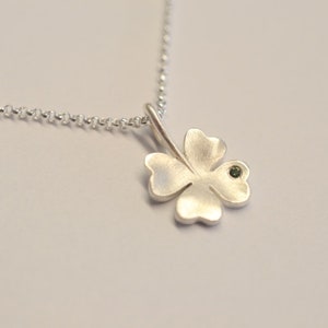Op de afbeelding: Een zilveren ketting met een klavertje vier hanger met een kleine groene edelsteen in het midden.