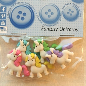 Può includere: Sei bottoni di plastica a forma di unicorno colorati con corpi bianchi e criniere e code di diversi colori. I bottoni sono confezionati in un sacchetto di plastica trasparente con una carta di intestazione blu e bianca che recita "Creative Button Assortments for Crafting. Cardmaking. Quilting. Sewing. Scrapbooking. Fantasy Unicorns."