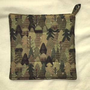 Puede incluir: Salvamanteles cuadrado acolchado con un diseño de escena de bosque. El patrón presenta varios árboles en tonos verdes, marrones y beige. Tiene un pequeño lazo para colgar y mide aproximadamente 20 cm cuadrados.