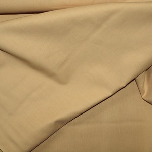Könnte beinhalten: Nahaufnahme eines glatten, hellbraunen Stoffes. Der Stoff ist gefaltet und hat eine weiche, natürliche Textur.
