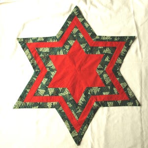 Può includere: Un tappetino in tessuto a forma di stella a sei punte con un centro in tessuto rosso a pois bianchi, circondato da un bordo rosso e uno strato esterno in tessuto verde scuro stampato con un motivo di alberi di pino bianchi.