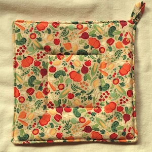 Peut inclure: Un dessous de plat carré beige avec un motif de légumes colorés. Le motif comprend des images de citrouilles, de tomates, de brocolis, de maïs et d'autres légumes. Il y a une petite boucle pour suspendre.