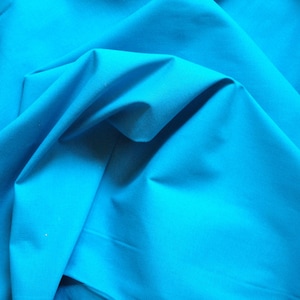 Puede incluir: Primer plano de una tela de color turquesa brillante, doblada y drapeada, mostrando su textura suave y su color vibrante.