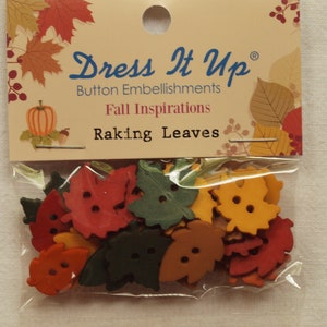 Könnte beinhalten: Eine Packung blattförmiger Knöpfe in Herbstfarben: Rot, Orange, Gelb und Grün. Die Packung ist mit "Dress It Up" und "Fall Inspirations: Raking Leaves" beschriftet.