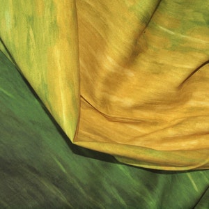 Può includere: Un primo piano di un tessuto con un gradiente di colori verde e giallo. Il tessuto è piegato e ha un aspetto morbido e testurizzato.