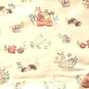 Könnte beinhalten: Ein hellbeiger Stoff mit einem sich wiederholenden Muster aus Waldtieren wie Füchsen, Igeln, Kaninchen, Eichhörnchen, Mäusen und Enten. Die Illustrationen sind in sanften Braun-, Orange- und gedämpften Grüntönen mit kleinen Schmetterlingen gehalten.
