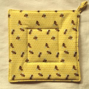 Könnte beinhalten: Gelber gesteppter Topflappen mit einem Wabenmuster und einem Bienendesign. Der Topflappen hat einen Schlaufe.