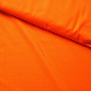 May include: A close-up of a bright orange fabric with a smooth texture. The fabric is folded in half, creating a diagonal crease.