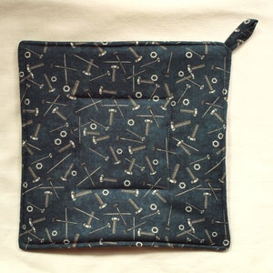 Op de afbeelding: Vierkante, donkerblauwe pannenlap met een patroon van zilverkleurige bouten, moeren en spijkers. De pannenlap heeft een kleine lus om op te hangen en een gewatteerd ontwerp. De randen zijn netjes afgewerkt met donkerblauwe bies. Ongeveer 20 cm x 20 cm.