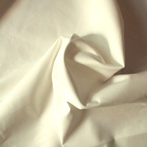 May include: A close-up of a white fabric with a smooth texture. The fabric is folded and draped, creating soft folds and curves.