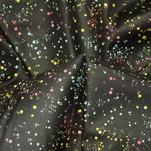 Puede incluir: Tela negra con un patrón de puntos coloridos en tonos rosa, amarillo, azul y blanco. Los puntos varían en tamaño y densidad, creando un efecto moteado en la superficie. La tela está doblada, mostrando la textura.