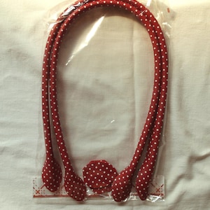 Può includere: Tre cinturini in tessuto rosso con pois bianchi e un cerchio in tessuto con pois abbinati. I cinturini sono confezionati in un sacchetto di plastica trasparente.