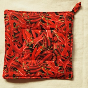 Op de afbeelding: Vierkante rode en zwarte pannenlap met een herhalend patroon van rode chilipepers. De pannenlap heeft een lus om op te hangen en is ontworpen voor gebruik in de keuken.