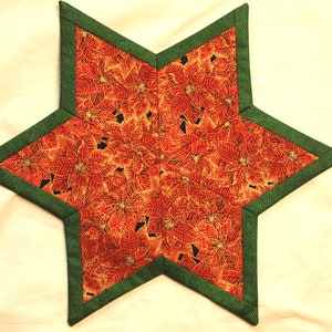 Könnte beinhalten: Ein sternförmiger, gesteppter Tischläufer mit einem Poinsettienmuster in Rot, Gold und Schwarz. Die Kanten sind mit grünem Stoff eingefasst. Eine festliche Dekoration für die Weihnachtszeit.