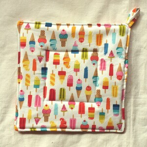 May include: A white cotton pot holder with a colorful ice cream cone and popsicle pattern. The pot holder has a loop handle.