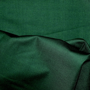 Puede incluir: Primer plano de una tela verde oscuro con una textura suave y sedosa. La tela está doblada y drapeada, creando pliegues y sombras suaves.
