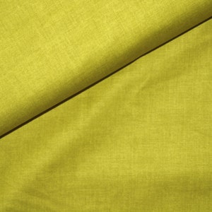 Puede incluir: Primer plano de una tela doblada en un vibrante color chartreuse. La tela tiene una apariencia texturizada, con hilos tejidos visibles. El pliegue diagonal crea un contraste de luz y sombra, resaltando la textura del material.
