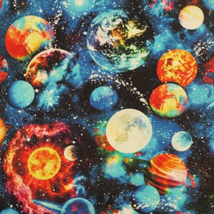 May include: A colourful fabric with a space theme. The fabric features a dark blue background with a variety of planets, stars, and nebulae. The planets are in various colours, including red, orange, yellow, green, and blue. The stars are white and the nebulae are pink and purple.