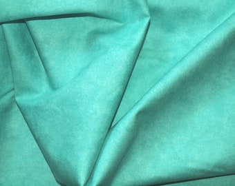 May include: Close-up of a folded piece of teal fabric. The fabric has a slightly textured appearance and is draped in soft folds, creating shadows and highlights. The color is a vibrant, medium teal.