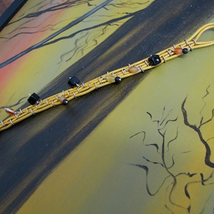 Könnte beinhalten: Ein gelbes Lederarmband mit schwarzen und braunen Perlen und silbernen Draht-Akzenten. Das Armband hat einen Schlaufenschluss.