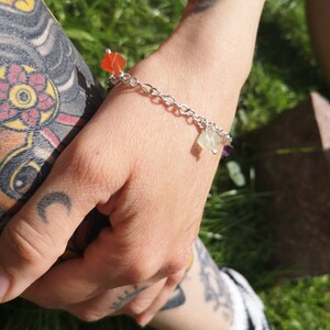 Könnte beinhalten: Ein silbernes Kettenarmband mit kleinen, bunten Edelstein-Anhängern. Das Armband befindet sich am Handgelenk einer Person, und die Anhänger sind sichtbar.
