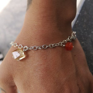 Könnte beinhalten: Ein silbernes Kettenarmband mit einem klaren Quarz-Anhänger und einem roten Karneol-Anhänger.