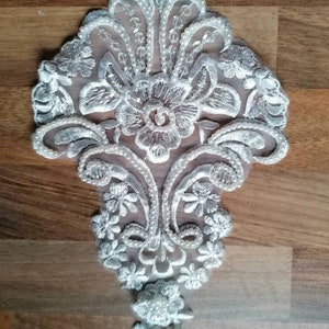 May include: White lace applique with pearl embellishments. The applique features a floral design with intricate details.