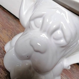 Könnte beinhalten: Weiße Keramik-Teekanne in Form eines Hundes mit Ausguss und Deckel. Die Teekanne steht auf einer Holzoberfläche.