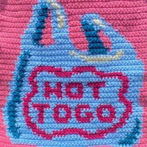 K&ouml;nnte beinhalten: Ein handgefertigtes, geh&auml;keltes Objekt mit einem hellblauen Taschen-Design mit einem rosa Rand und den Worten "HOT TOCO" in Rosa. Der Hintergrund ist einfarbig rosa.