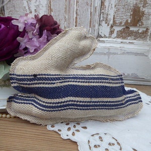 May include: A handmade fabric bunny toy with a white and blue striped pattern. The bunny is made of a natural linen fabric and has a simple, rustic design.