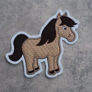 Könnte beinhalten: Ein braunes und weiß gepunktetes Pferde-Applikationsmotiv mit brauner Mähne und Schweif. Das Pferd steht auf allen vieren und hat einen weißen Umriss.