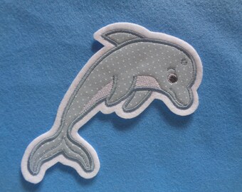 Könnte beinhalten: Ein grauer Filz-Delfin mit weißen Nähten und einem weißen Umriss. Der Delfin hat ein gepunktetes Muster und ein schwarzes Auge.