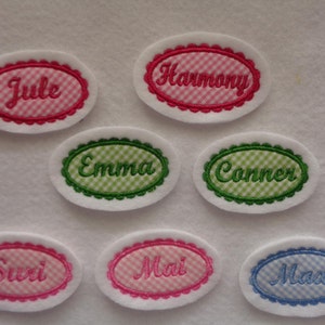 Könnte beinhalten: Sieben ovale gestickte Patches mit Gingham-Mustern und Namen in Kursivschrift. Die Namen sind: Jule, Harmony, Emma, Conner, Suri, Mai und Max. Die Patches sind weiß mit rosa, grünen und blauen Gingham-Mustern.
