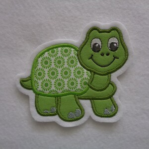 Könnte beinhalten: Grünfilz-Applikation einer lächelnden Schildkröte mit einem grün-weiß gemusterten Panzer.