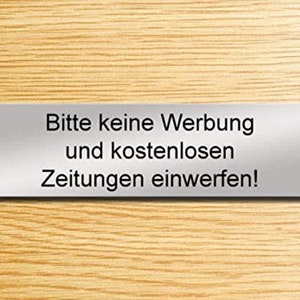 Op de afbeelding: Een zilveren bord met de tekst "Bitte keine Werbung und kostenlosen Zeitungen einwerfen!" wat vertaald wordt naar "Gooi geen reclame en gratis kranten weg!"