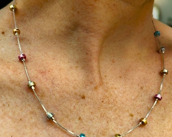 May include: A silver chain necklace with colorful round beads. The beads are in shades of gold, pink, and blue.
