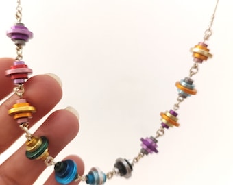 May include: A silver chain necklace with colorful stacked disc pendants. The discs are in shades of purple, red, orange, yellow, green, blue, and gray.
