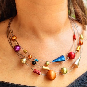 May include: A multi-strand necklace with a variety of colorful beads and geometric shapes. The necklace features a blue cone, a silver cone, and round beads in shades of orange, red, purple, green, and gold.