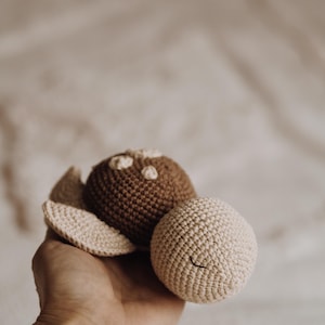 May include: A crocheted turtle toy with a brown shell and a cream-colored belly. The turtle has a simple embroidered face.