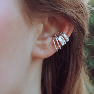 Puede incluir: Un pendiente de oreja de plata con múltiples anillos, usado en la parte superior de la oreja.