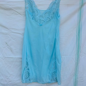 以下が含まれることがあります： 首元と裾に白いレースのトリムが付いた、薄い水色のスリップドレスです。