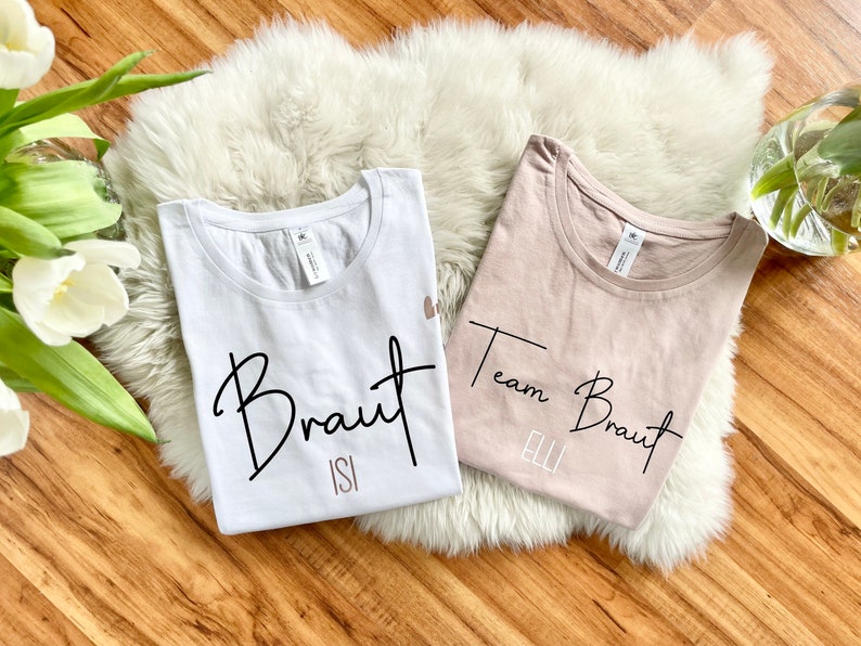 Pode incluir: Duas camisetas brancas com texto preto. Uma camiseta diz "Braut Isi" e a outra diz "Team Braut Elli".