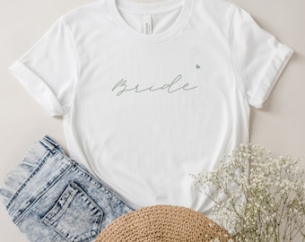 May include: White t-shirt with the word "bride" written in cursive in light green with a small heart above the word.