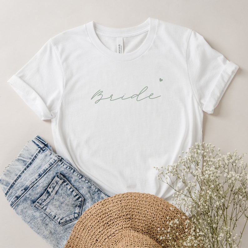 Pode incluir: Camiseta branca com a palavra "bride" escrita em it&aacute;lico em verde claro com um pequeno cora&ccedil;&atilde;o acima da palavra.