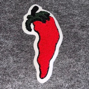 May include: A red chili pepper patch with a white border and green and black details. The patch is embroidered and has a textured appearance. The pepper shape is a classic design, perfect for adding to clothing or accessories.